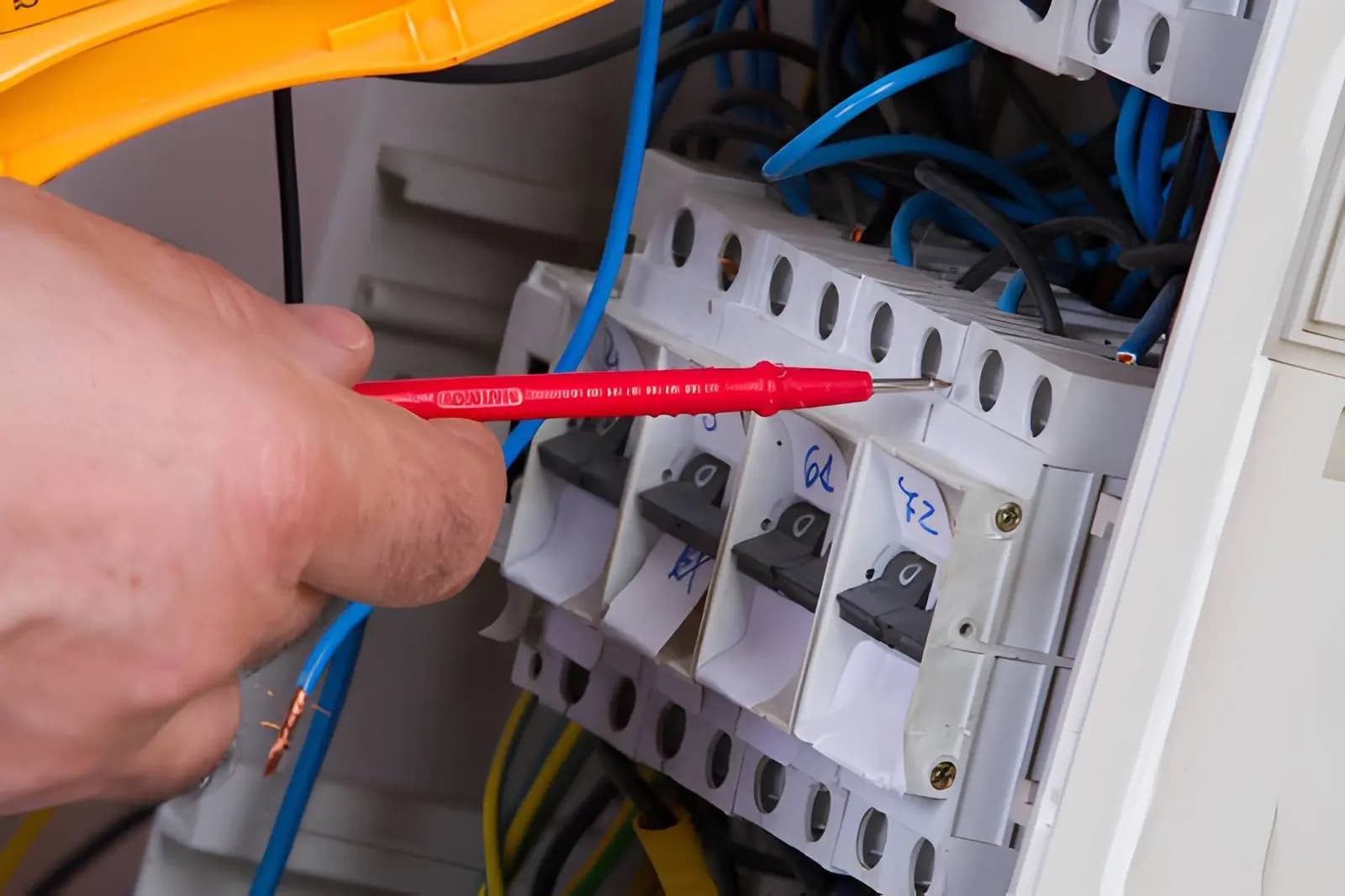 Electrician testing circuit breakers inside an electrical panel with a voltage tester