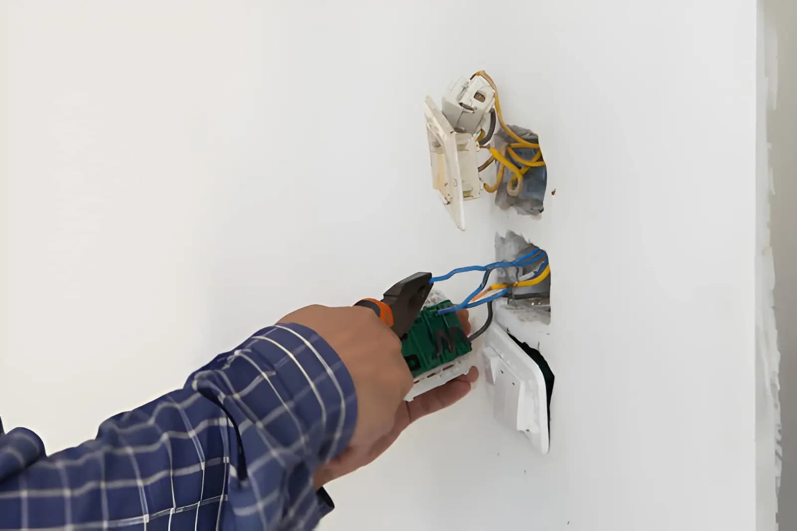 Electrician repairing wiring behind a wall outlet in a home